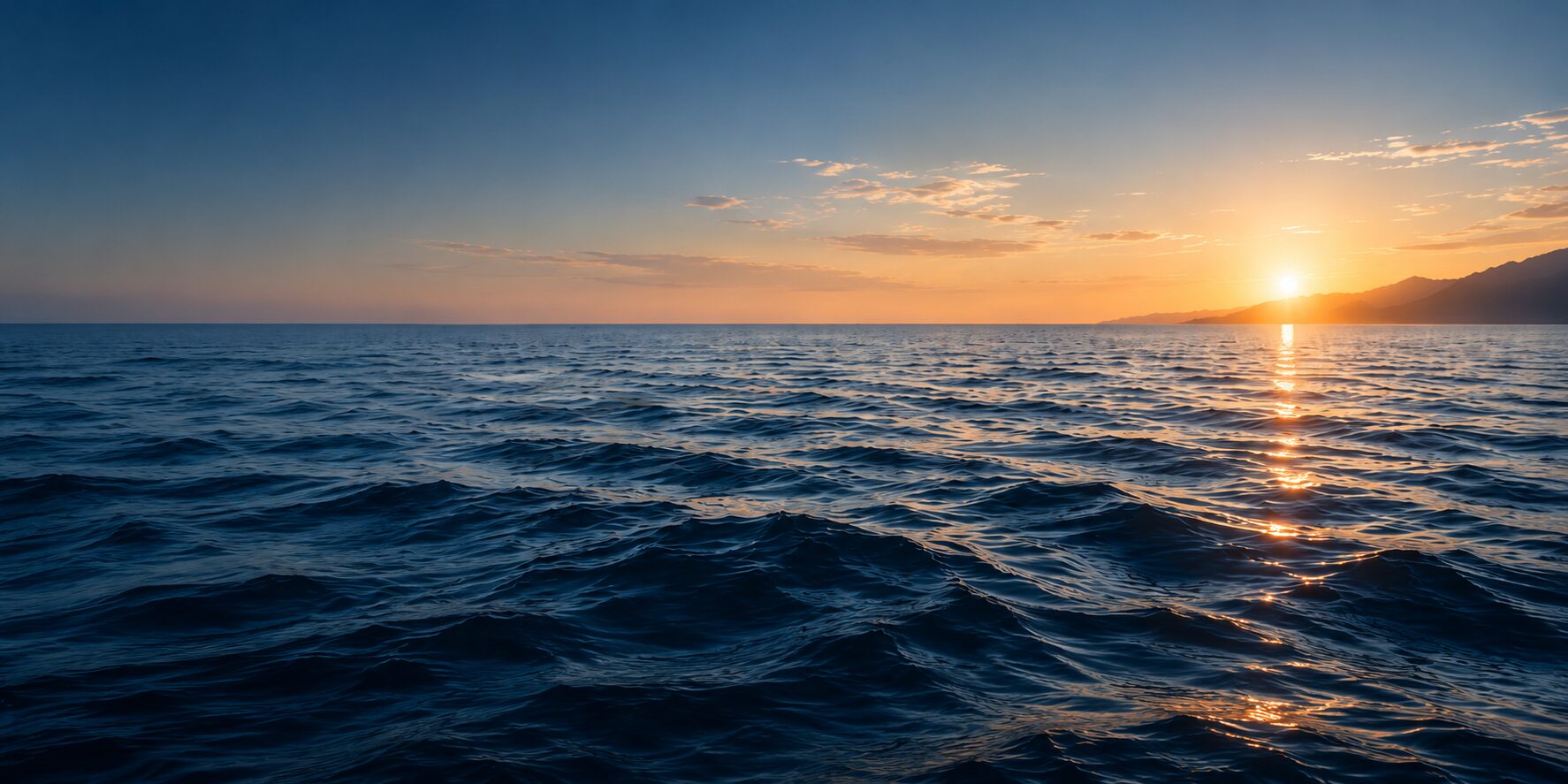 A calm ocean at sunset with gold light on the horizon